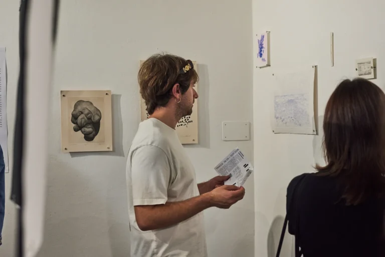 Un visitatore con il foglio di sala davanti alle stampe in parete